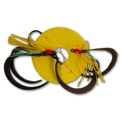 A fishing lure set featuring a bright yellow circular skirt, dark brown paddle tails, yellow and green skirt strands, and red bead accents on a white background.